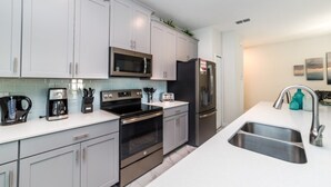A modern kitchen with white cabinets, stainless steel appliances, and a double sink. - Rent a Luxury Townhome on Storey Lake Resort, Minutes From Disney, Orlando Townhome 1004 (Kissimmee)