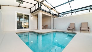 An indoor swimming pool with a clear blue water, surrounded by a white tiled floor and walls. There are two lounge chairs and a table with chairs outside the pool area. - Rent a Luxury Townhome on Storey Lake Resort, Minutes From Disney, Orlando Townhome 1004 (Kissimmee)