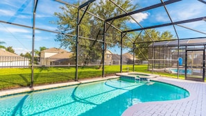 A swimming pool with a glass enclosure, surrounded by a well-maintained lawn and a fence.