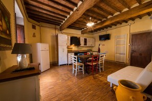 Una cucina compatta con travi in legno, un'area pranzo con sedie, un divano bianco e una pentola gialla.