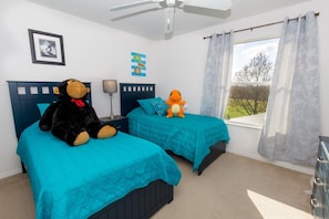 A bedroom with two beds, a ceiling fan, a window with curtains, and a framed picture on the wall.