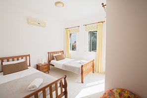 A hotel room with two single beds, a small bedside table with a lamp, a window with curtains, and a wall-mounted air conditioner. - Cyprus Villa Near the Beach, Paralimni Villa 1308 (Paralimni)