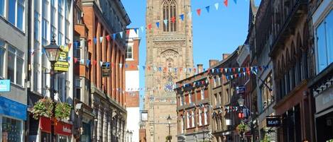 A street with historic buildings, a prominent clock tower, and a clear blue sky.