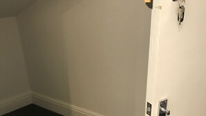 Een kamer met een witte deur, een donker vloerkleed en een witte muur.