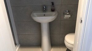 Een badkamer met een wastafel op voetstuk, toilet en een handdoekrek.