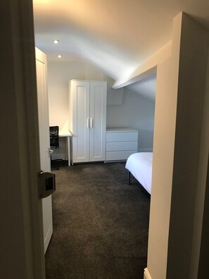 A small, dimly lit room with a single bed, a white wardrobe, and a desk with a chair. - Self Contained Studio (Derby)