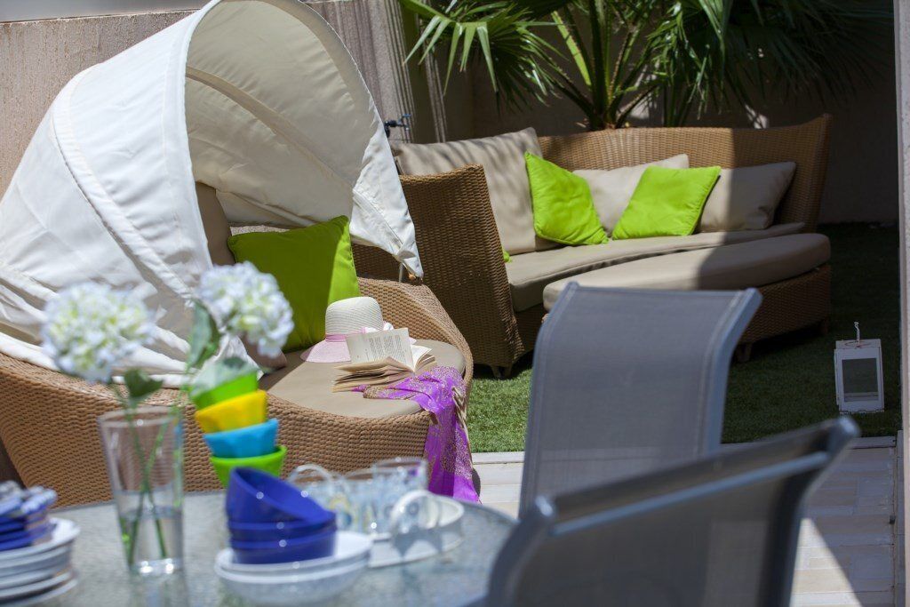 Een terras met rieten meubels, een overdekte tafel en een kleine tuin.