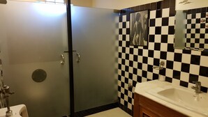 A bathroom with a glass shower door, a sink with a mirror, and a checkered tile backsplash. - Cozy Cabin - Hostel (Bangkok)