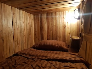 A wooden-paneled room with a bed, a nightstand, and a window.
