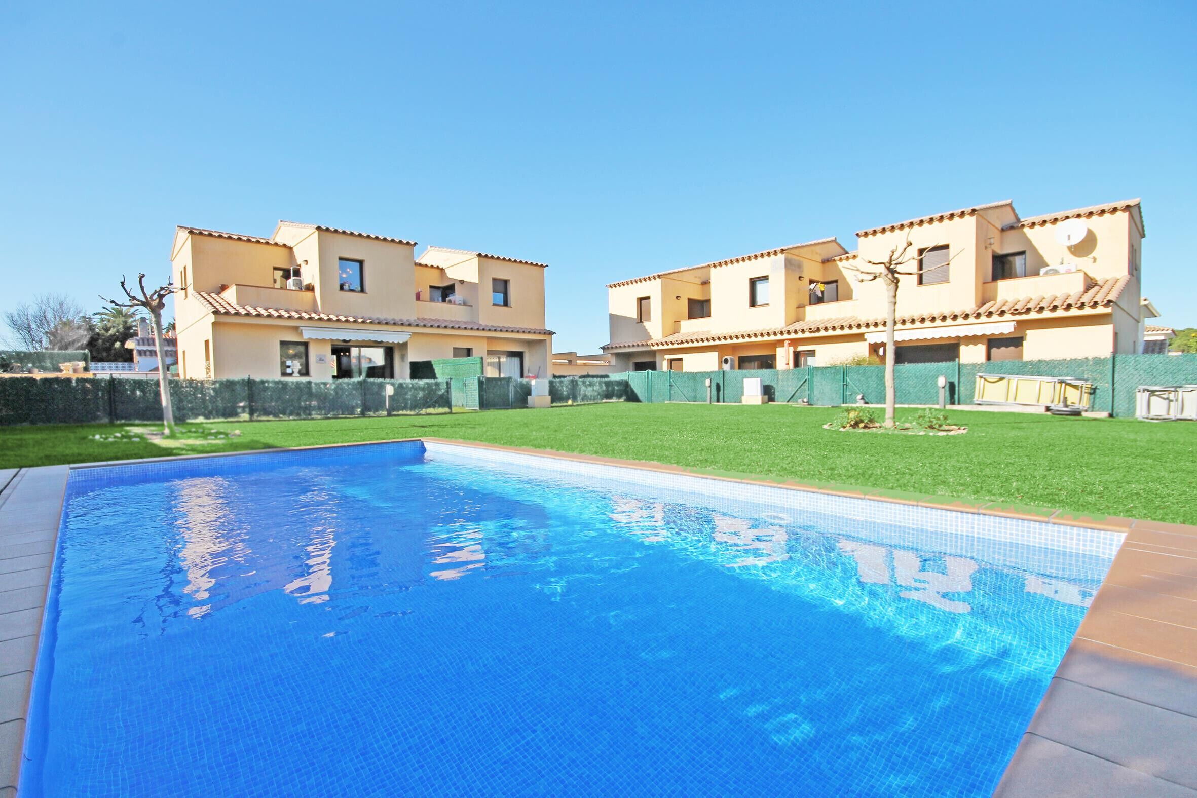A swimming pool with a tiled deck, surrounded by a well-maintained lawn and a two-story building with a tiled roof.