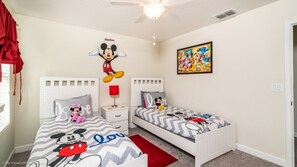 Une chambre d’enfant avec deux lits, chacun décoré avec des motifs de Mickey et de Minnie Mouse, un autocollant mural représentant Mickey Mouse et un tableau coloré sur le thème de Disney.