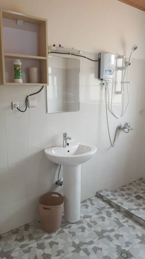 A bathroom with a pedestal sink, a mirror, a shower, and a shelf with toiletries. - Kigalicious (Kigali)