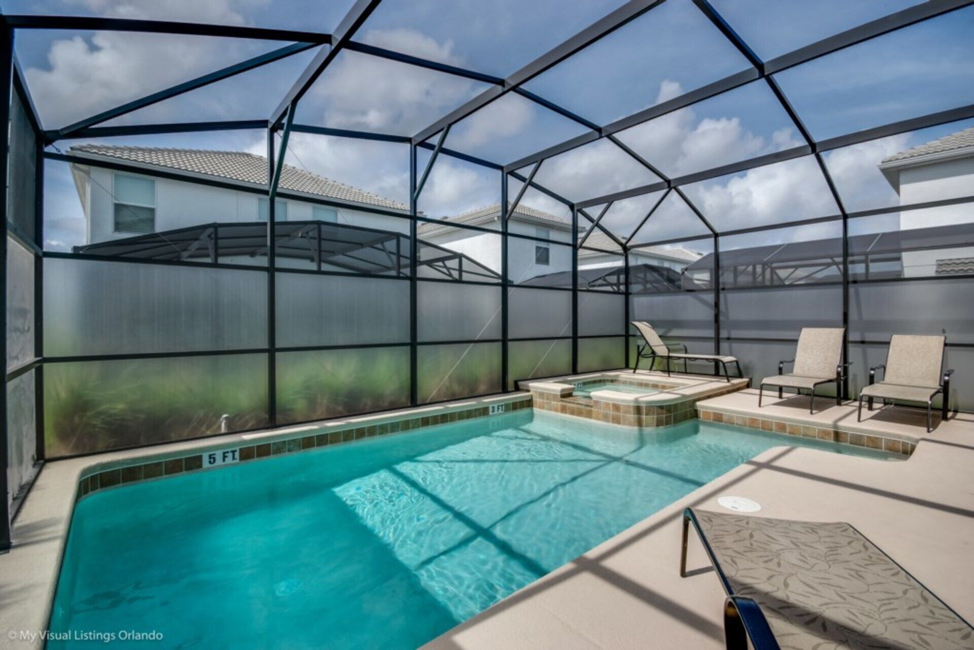 An indoor swimming pool with a glass enclosure, lounge chairs, and a hot tub.