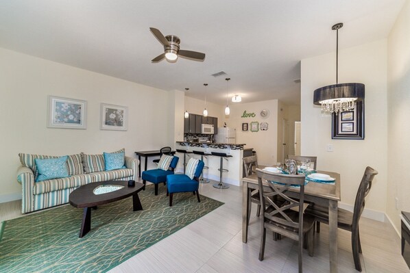 A modern living room with a sofa, coffee table, and a fireplace. There is a kitchen area with a dining table and chairs.