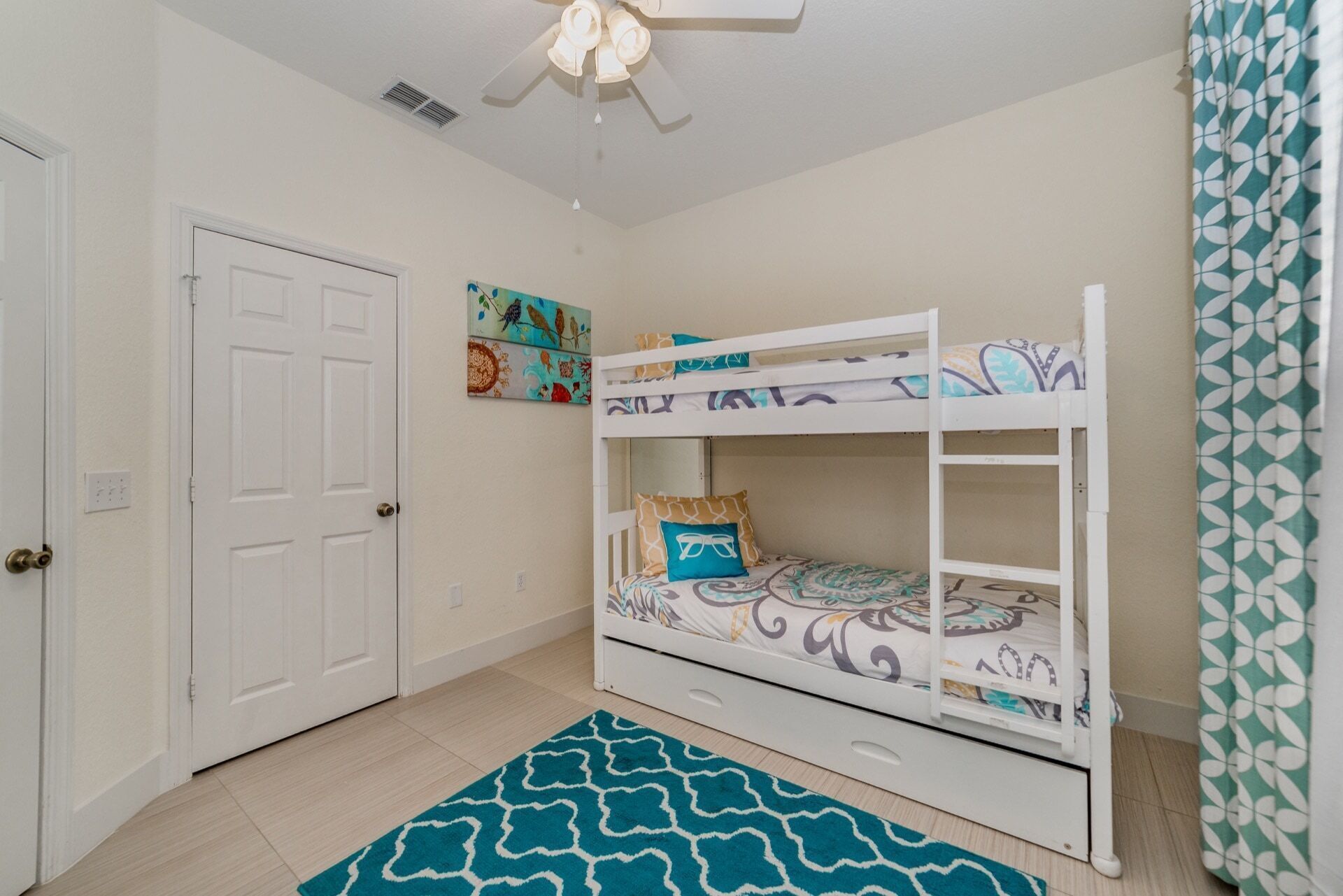 A room with a bunk bed, a door, a ceiling fan, and a patterned rug.