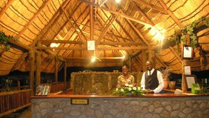 A reception area with a stone counter, wooden beams, and a thatched roof. - Ravine Lodge (Livingstone)