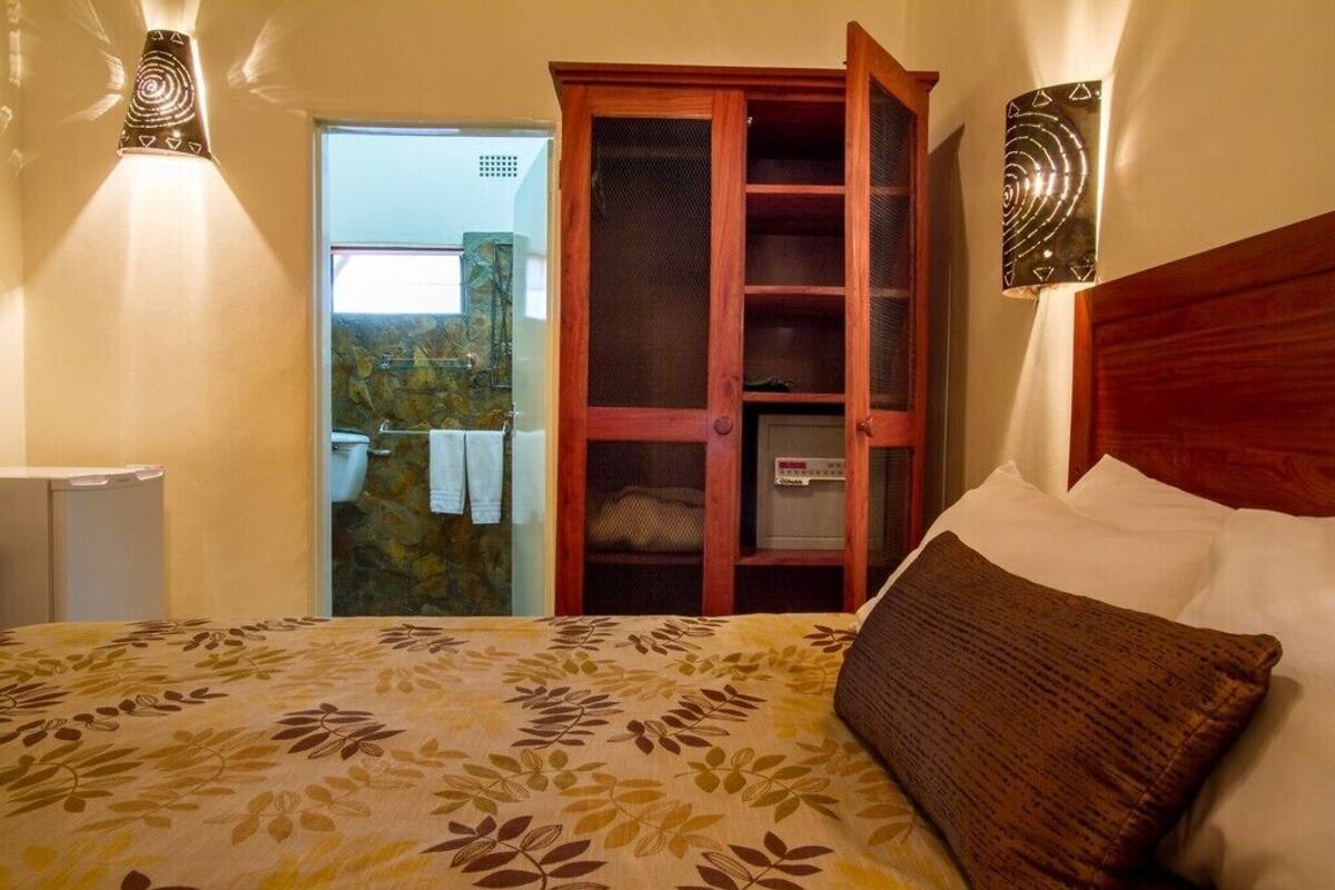 Quarto com cama, guarda-roupa de madeira e banheiro visível por uma porta aberta.
