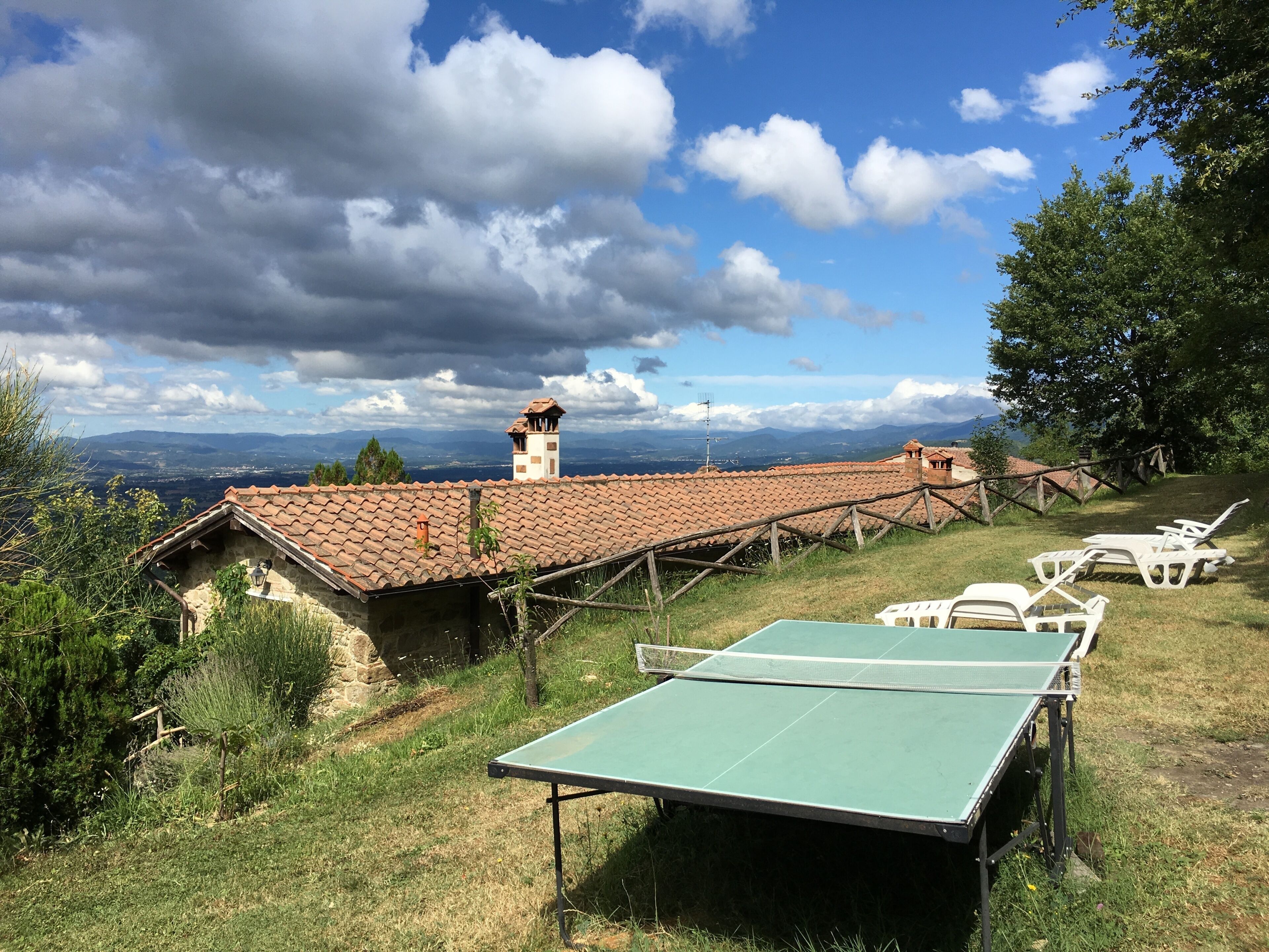 Un espacio al aire libre rústico con mesa de ping pong, sillones de descanso y un edificio de piedra con tejado de baldosas.