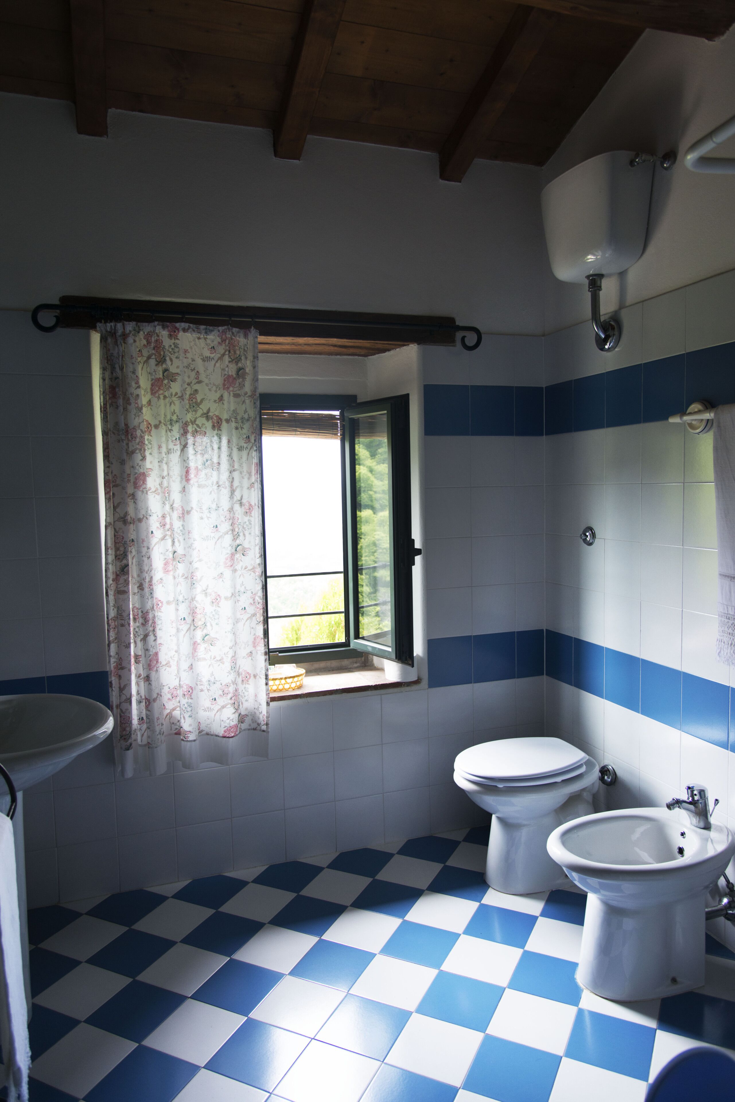 A bathroom with a checkered floor, a window with a floral curtain, and a sink.