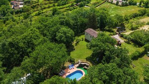 Vue aérienne d’un village à l’architecture traditionnelle, entouré d’une végétation luxuriante et doté d’un espace piscine.