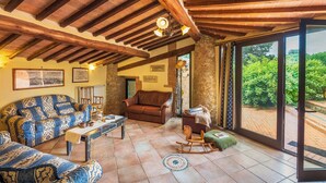 Un vaste salon doté d’un haut plafond en bois, d’une grande fenêtre offrant une vue sur la verdure et d’un coin salon confortable avec des canapés à motifs et un fauteuil à bascule.