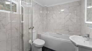 Et moderne badeværelse med brusekabine i glas, et hvidt toilet og et fritstående badekar.