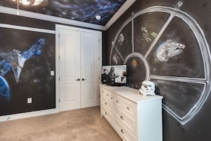 Ett rum med en väggmålning med Star Wars-tema, en vit byrå och en tv som visar en scen från en film.