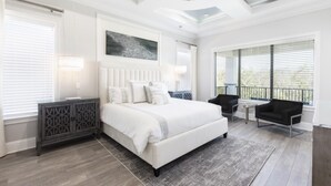 Ein modernes Schlafzimmer mit einem großen Bett, einem kleinen Tisch, zwei Stühlen und Blick auf einen Balkon.