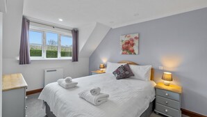 Une chambre à coucher avec un grand lit, deux tables de chevet avec des lampes, un radiateur et une fenêtre avec des rideaux.