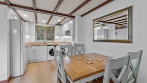 Une cuisine avec des meubles blancs, une table en bois et un grand miroir au mur.