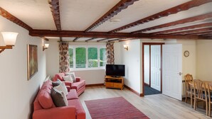 Un salon avec un canapé rouge, un téléviseur à écran plat posé sur un meuble en bois, un tapis à motifs et un coin repas comprenant des chaises et une table en bois.