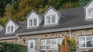 Une maison en pierre avec un toit à pignon, de nombreuses fenêtres et un petit porche.