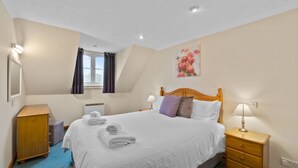 Une chambre d’hôtel avec un grand lit, une table de chevet en bois, une commode et un tableau au mur.