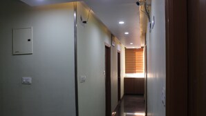 A hallway with a wooden door at the end, a light switch, and a smoke detector on the wall. - Olivia Inn And Suites (Bengaluru)