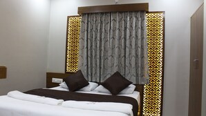 A neatly made bed with white linens and two dark pillows, a wooden headboard, and a patterned curtain. - Olivia Inn And Suites (Bengaluru)