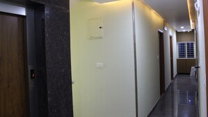 A hallway with a wooden door, a light switch, and a security camera on the wall. - Olivia Inn And Suites (Bengaluru)