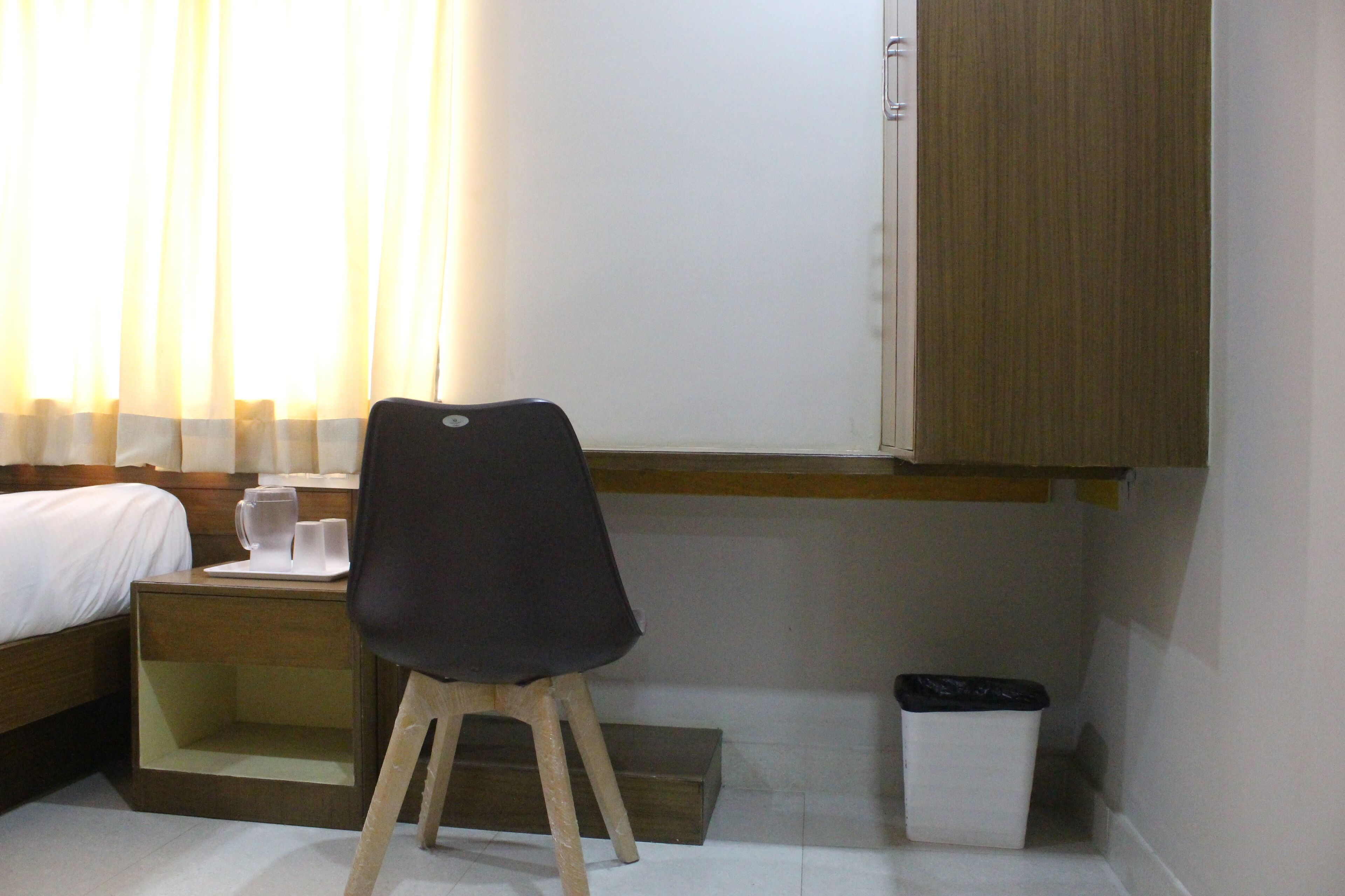 A hotel room with a bed, a desk with a chair, a trash bin, and a wooden cabinet.