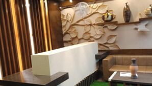 A reception area with a reception desk, a sofa, a coffee table, and a decorative wall with leaf patterns. - Olivia Inn And Suites (Bengaluru)