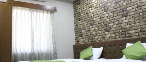 A hotel room with two beds, a stone wall, a window with curtains, and an air conditioning unit.