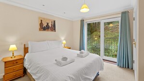 Quarto com uma cama grande, duas mesas de cabeceira com abajures, um quadro na parede e uma janela com cortinas.