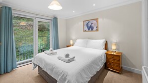Une chambre à coucher avec un grand lit, deux tables de chevet avec des lampes, une fenêtre avec des rideaux et un tableau accroché au mur.