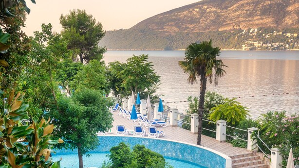 Un espace piscine doté de chaises longues et de parasols, entouré de verdure et offrant une vue sur une étendue d’eau.