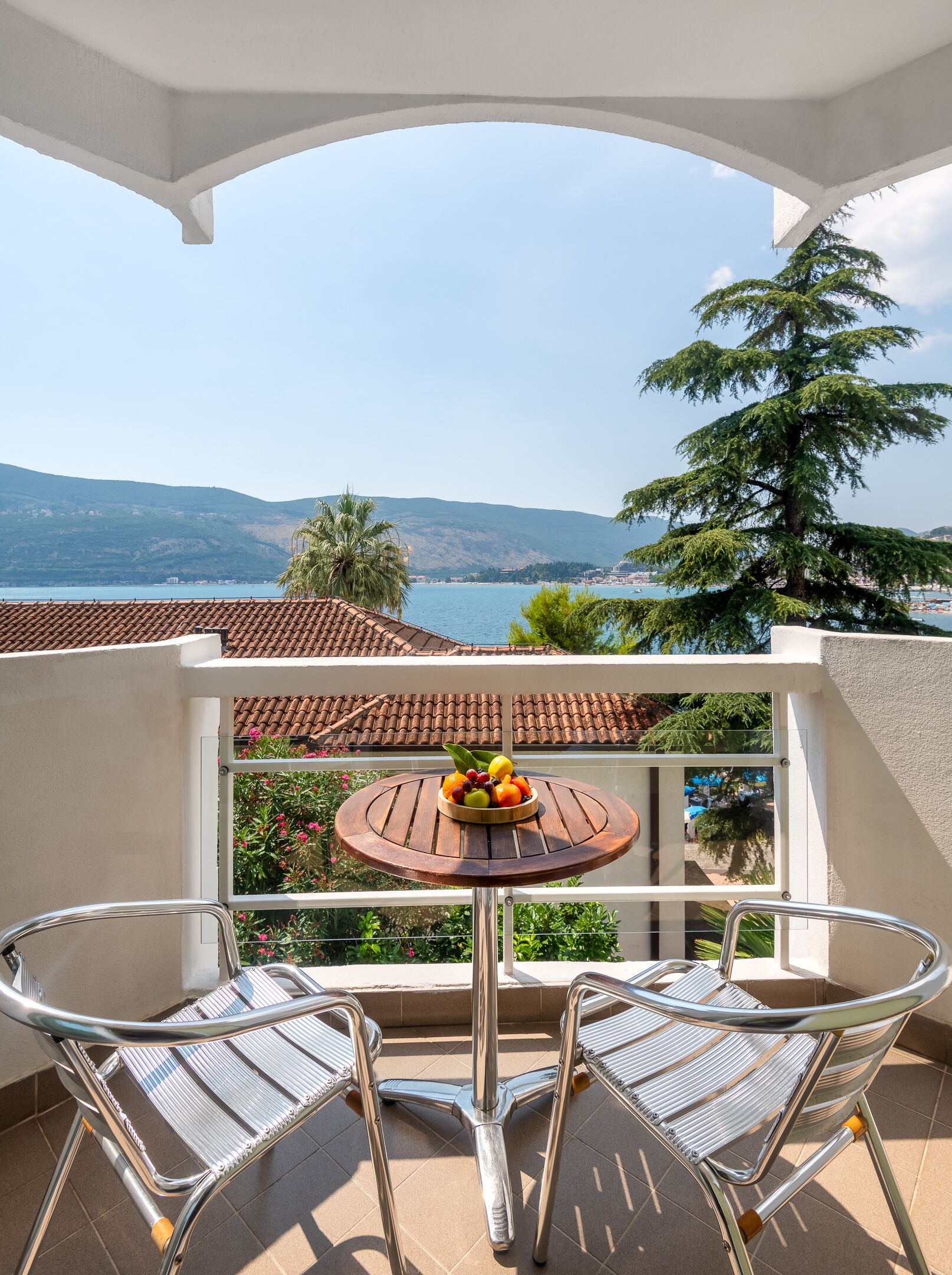 A balcony with a round table and two chairs, overlooking a scenic view of a lake and mountains.