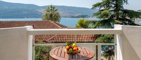 A balcony with a round table and two chairs, overlooking a scenic view of a lake and mountains.