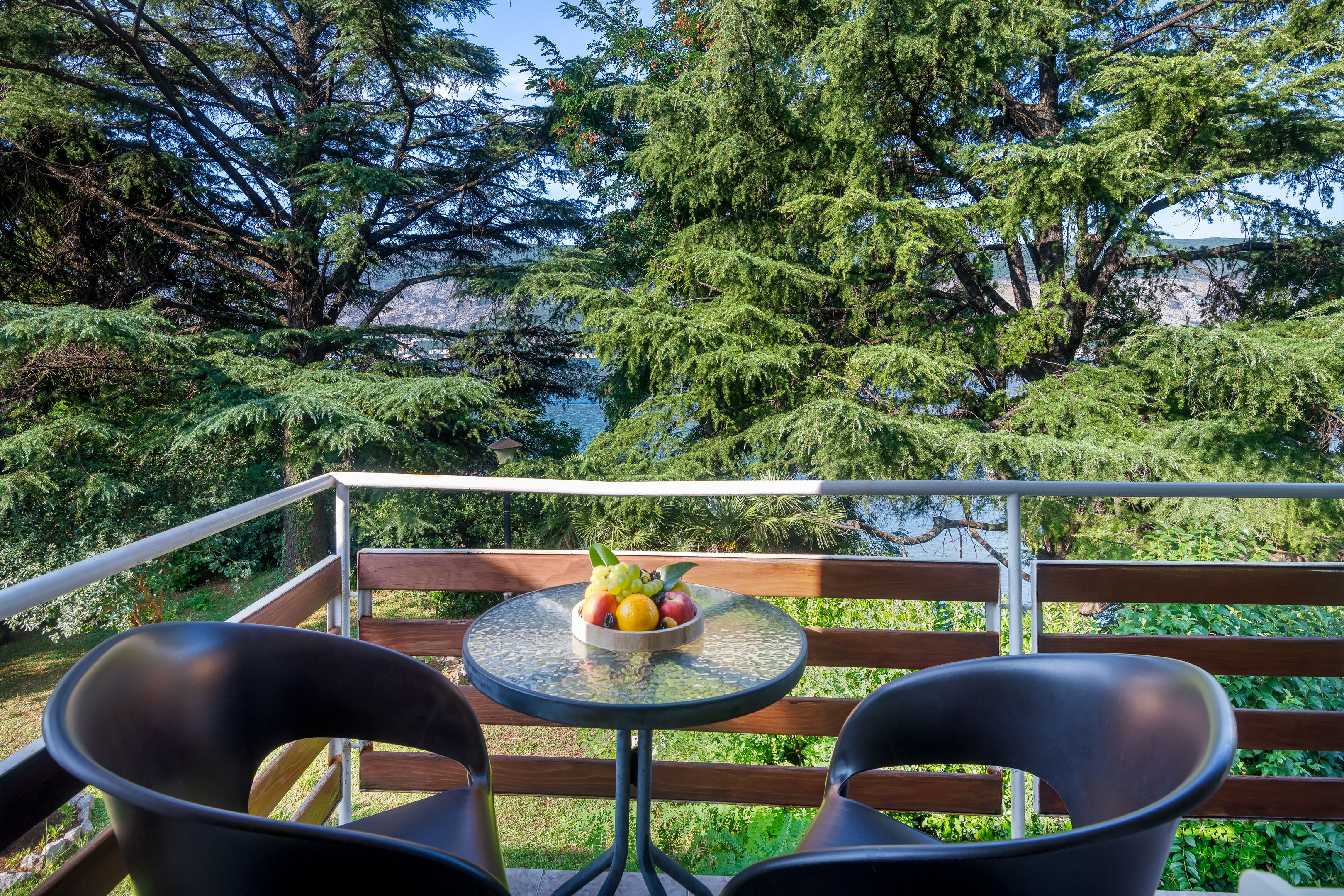 A balcony with two black chairs, a small round table, and a bowl of fruit.