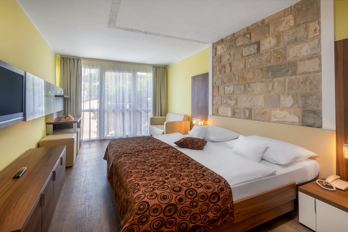 Ein Hotelzimmer mit einem großen Bett, einem Schreibtisch mit Fernseher, einer Steinwand und Blick ins Freie.