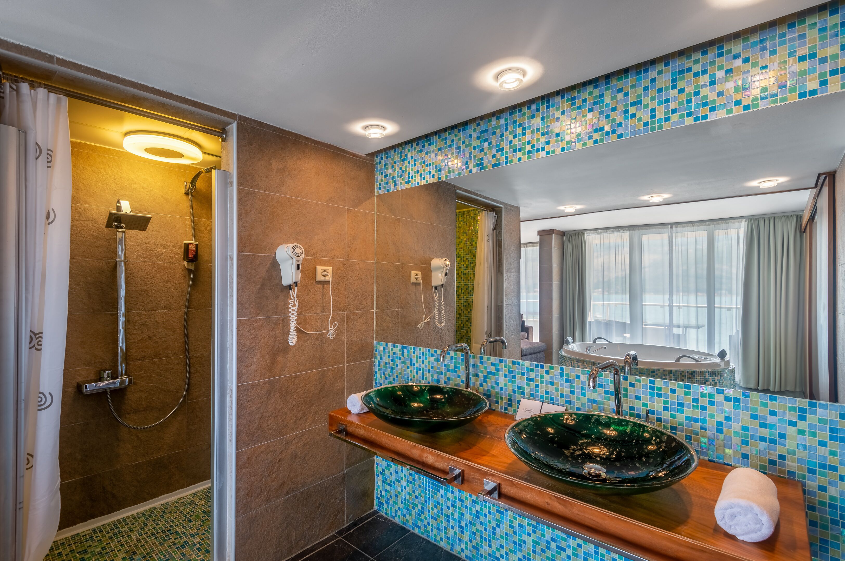 A modern bathroom with a glass-enclosed shower, two sinks with mosaic tile backs, and a large mirror.