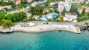 Vue aérienne d’un hôtel situé sur la côte, avec une piscine, des chaises longues et des parasols.