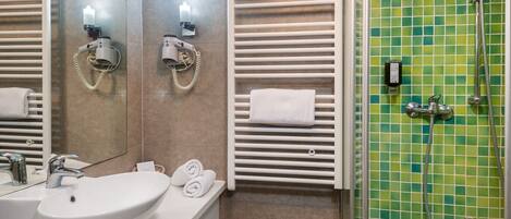 A modern bathroom with a large sink, two hair dryers, a towel rack, and a shower with a green mosaic wall.