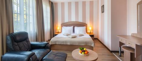 Habitación de hotel con cama, un sillón de cuero, una mesita redonda con fruta y un escritorio con cajones.